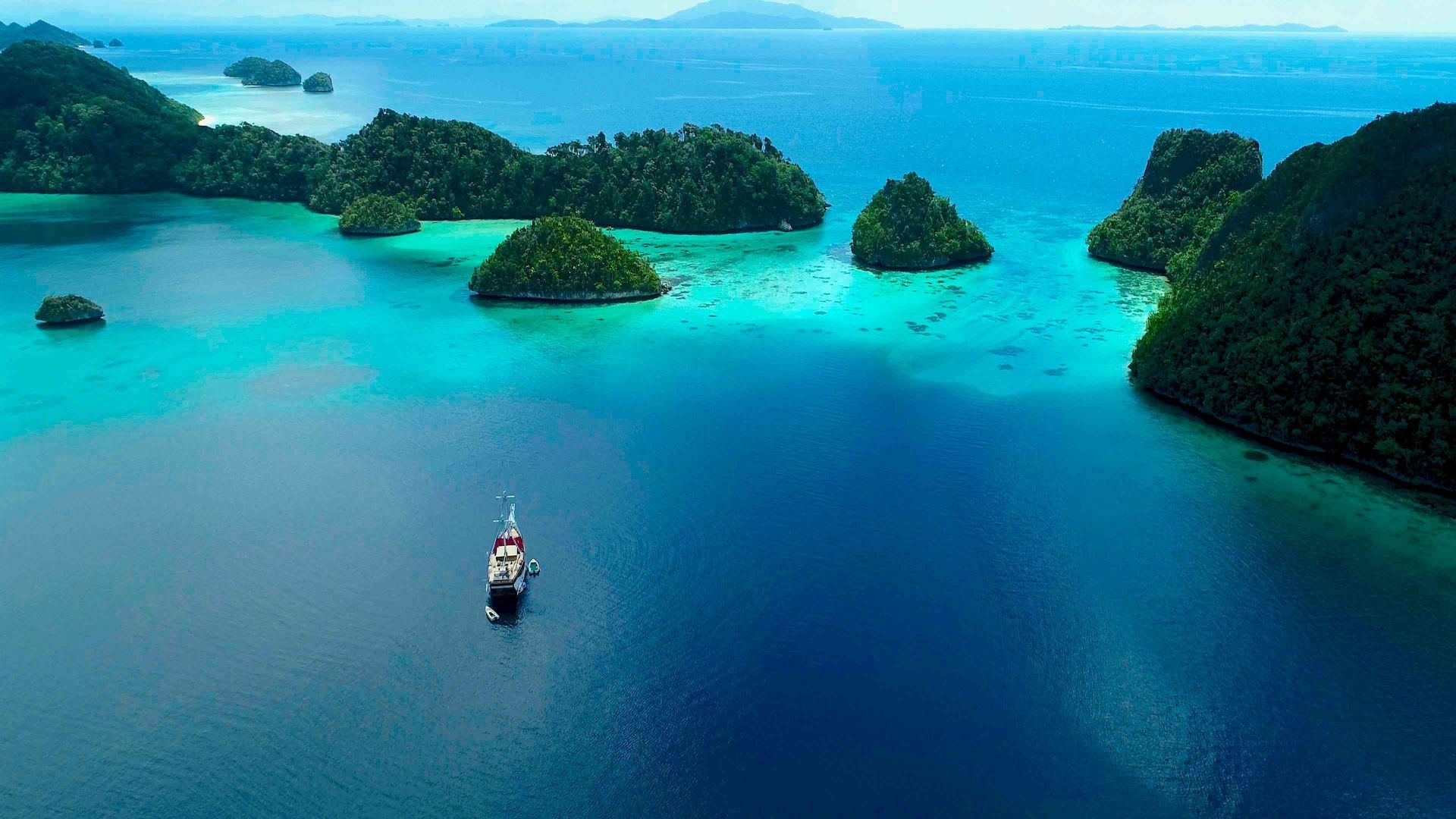 Aerial view of liveaboard vessel surrounded by mushroom-shaped karst islands in Raja Ampat West Papua