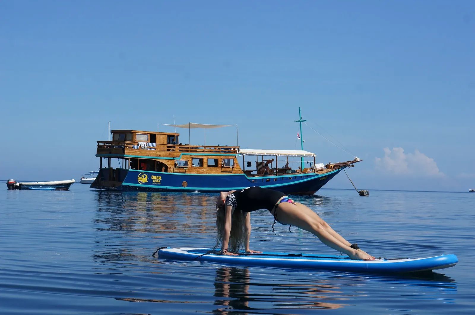 Amalia liveaboard – guest doing a yoga pose on a paddleboard near the vessel – Komodo, Indonesia