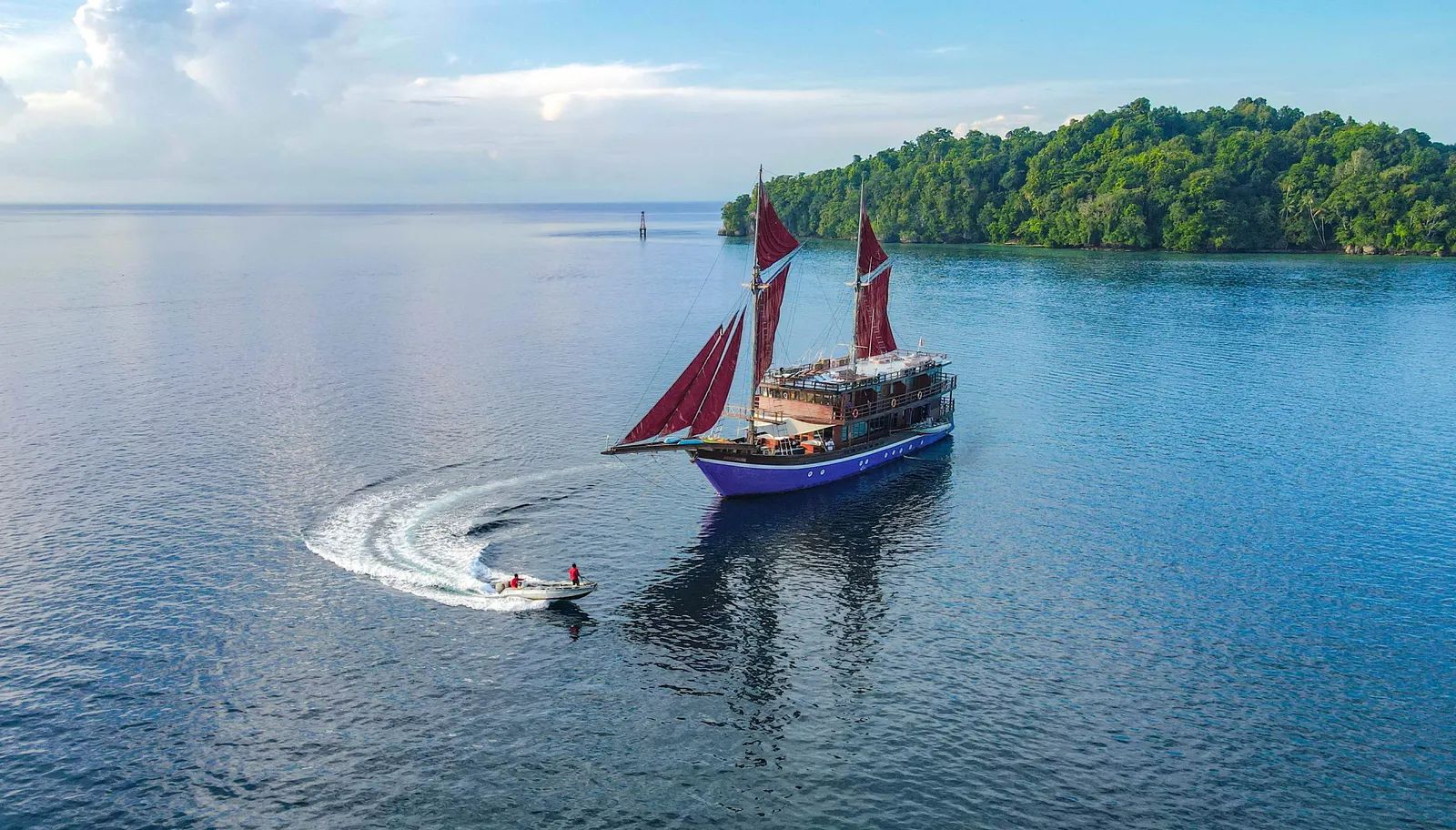 Neomi Cruise liveaboard – Phinisi schooner under sail with a tender boat turning in the foreground – Indonesia