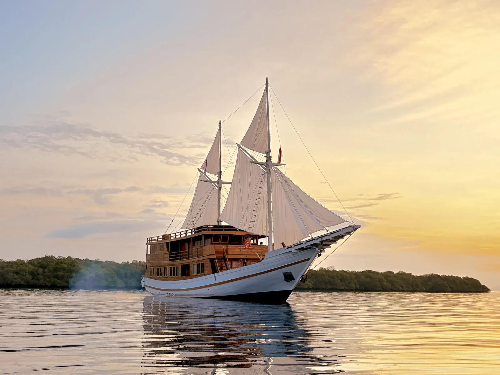 Sundari Voyages liveaboard – phinisi under sail at sunset near mangrove coast – Komodo, Indonesia